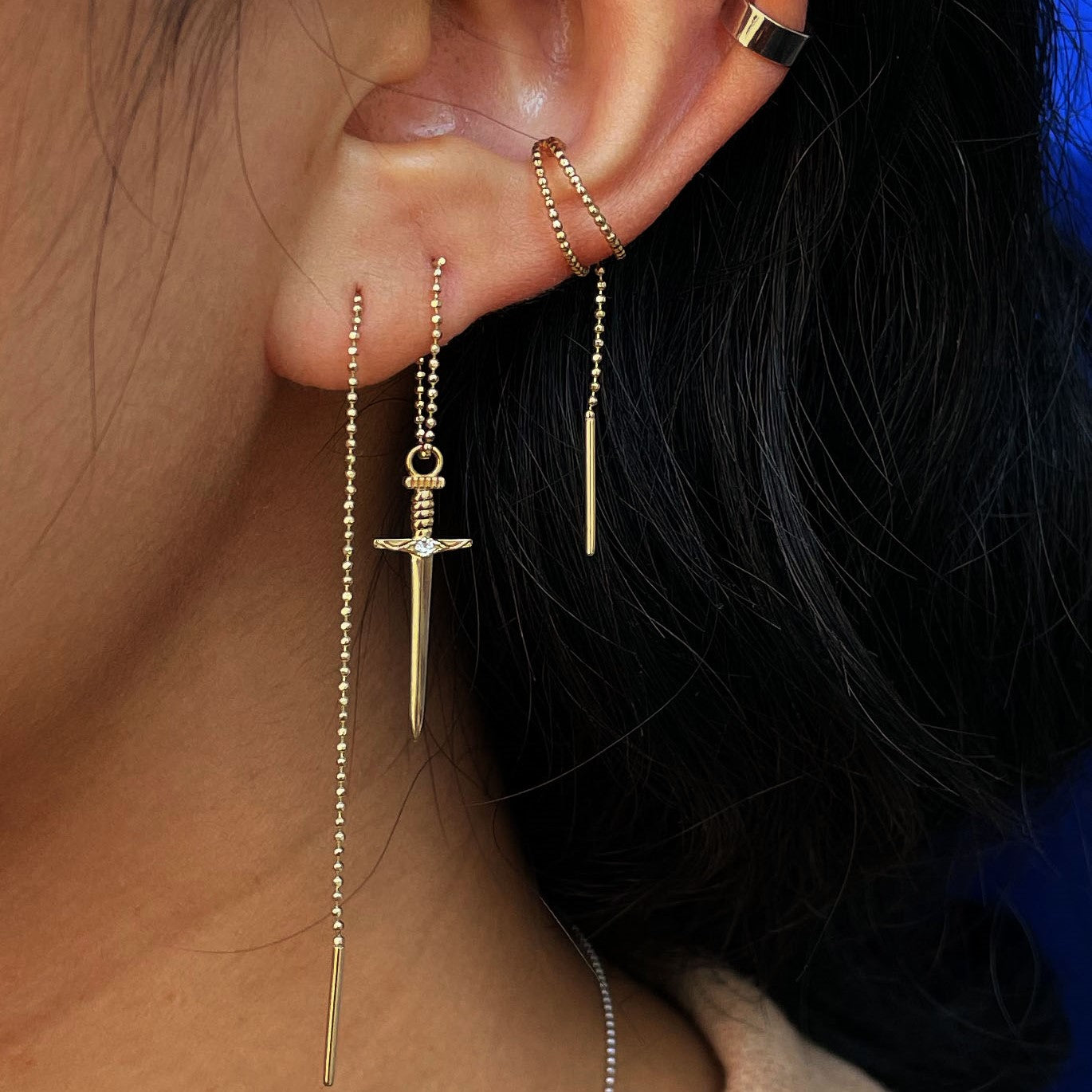 Close up view of a model's ear wearing a Sword Charm on a yellow gold Threader
