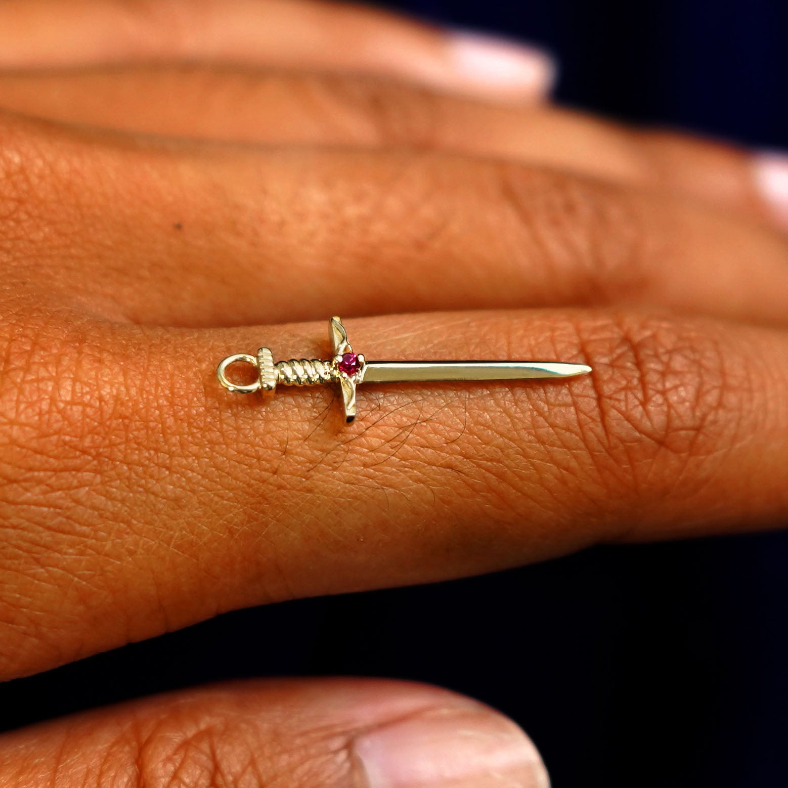 A 14k yellow gold ruby Sword Charm for earring balancing on the back of a model's finger