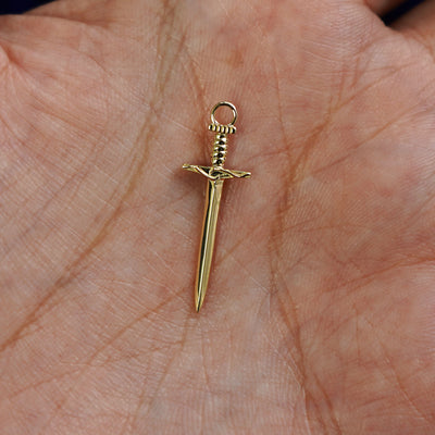 A 14k gold Sword Charm for earring resting in a model's palm to show the underside of the charm
