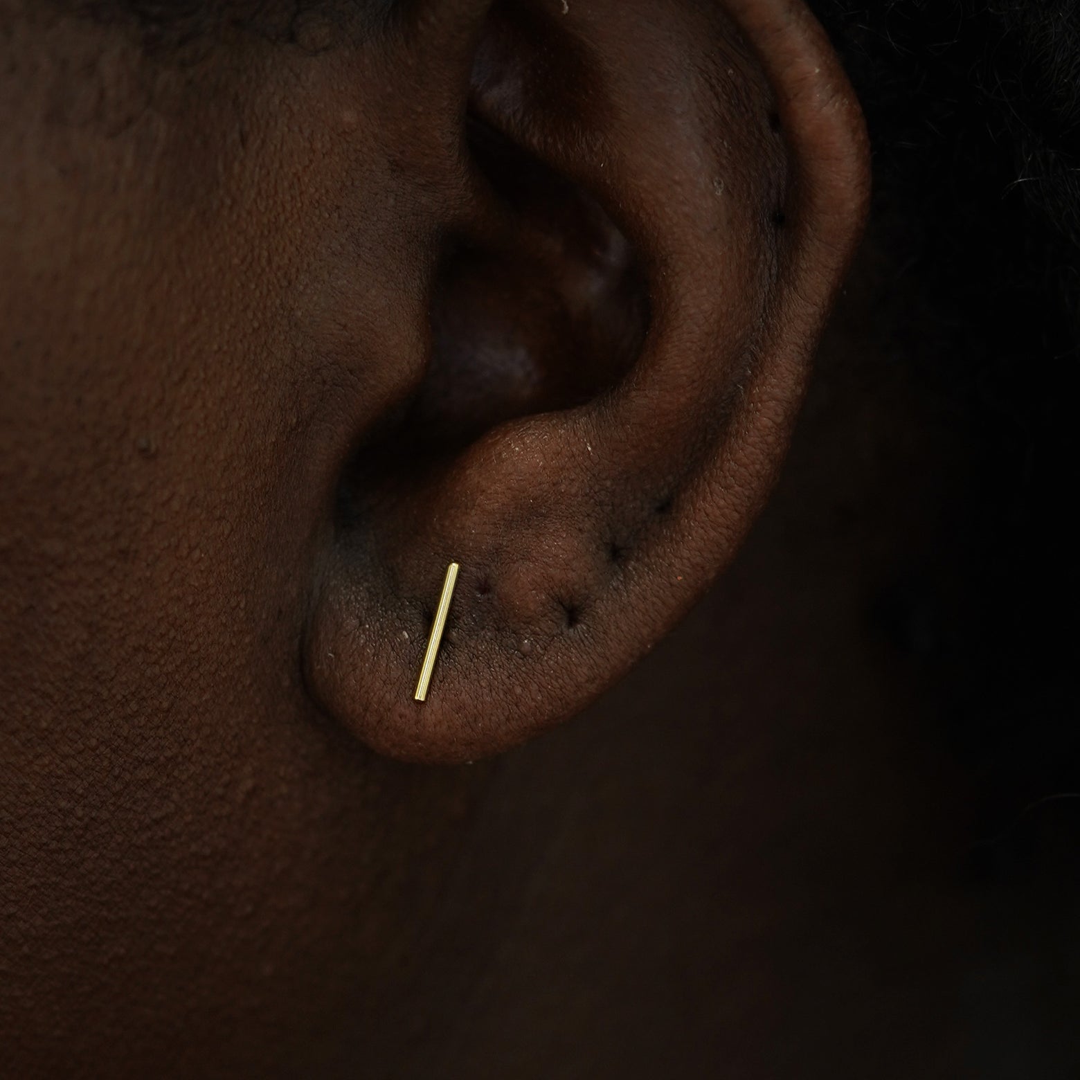 A model's ear wearing a 14k yellow gold Large Line Earring