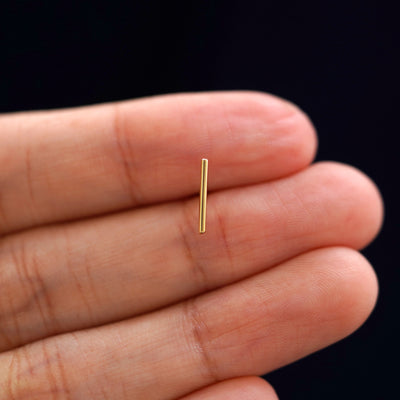 A solid 14k yellow gold Large Line Earring in between a model's fingers