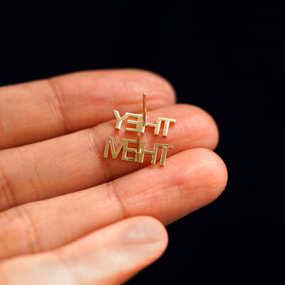A pair of yellow gold They / Them Earrings laying facedown on a model's fingers to show the underside view