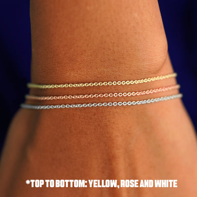 Close up view of a model's wrist wearing a three versions of the Thick Cable Bracelet in yellow, white, and rose gold