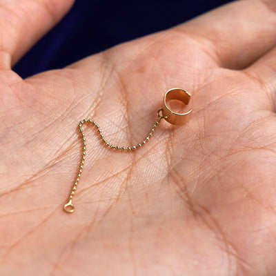 A solid yellow gold Thick Cuff with chain connector earring resting in a model's palm