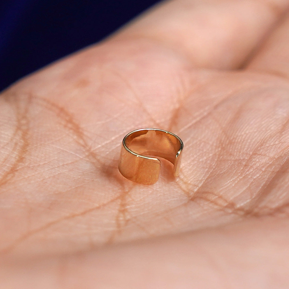 A solid yellow gold Thick Cuff earring resting in a model's palm