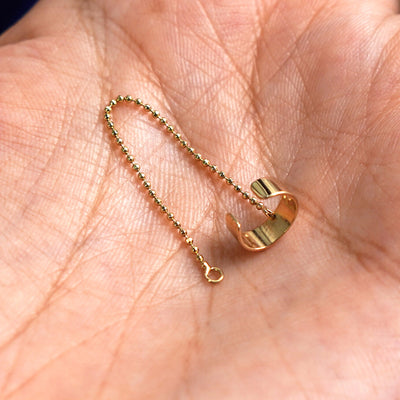 A solid yellow gold Thick Cuff with chain standing upright in a model's palm