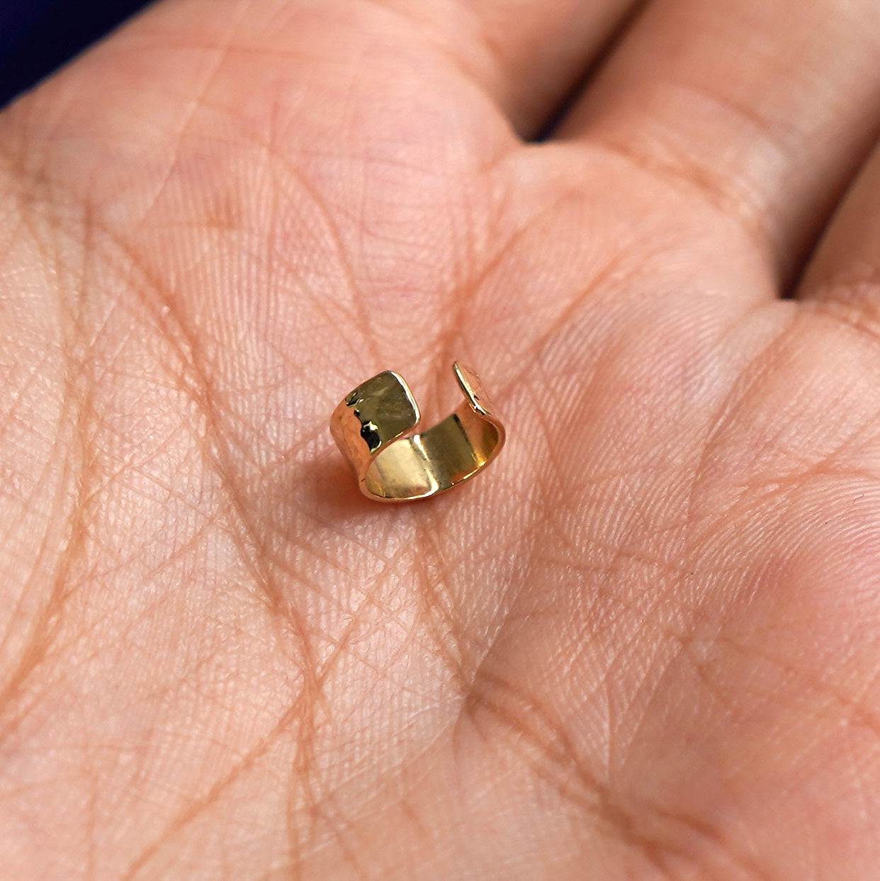 A solid yellow gold Thick Hammered Cuff earring standing upright in a model's palm