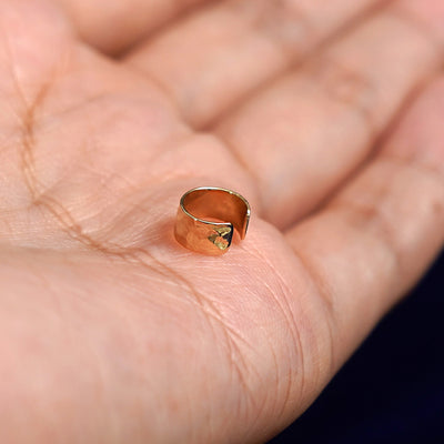 A solid yellow gold Thick Hammered Cuff earring resting on the edge of a model's palm