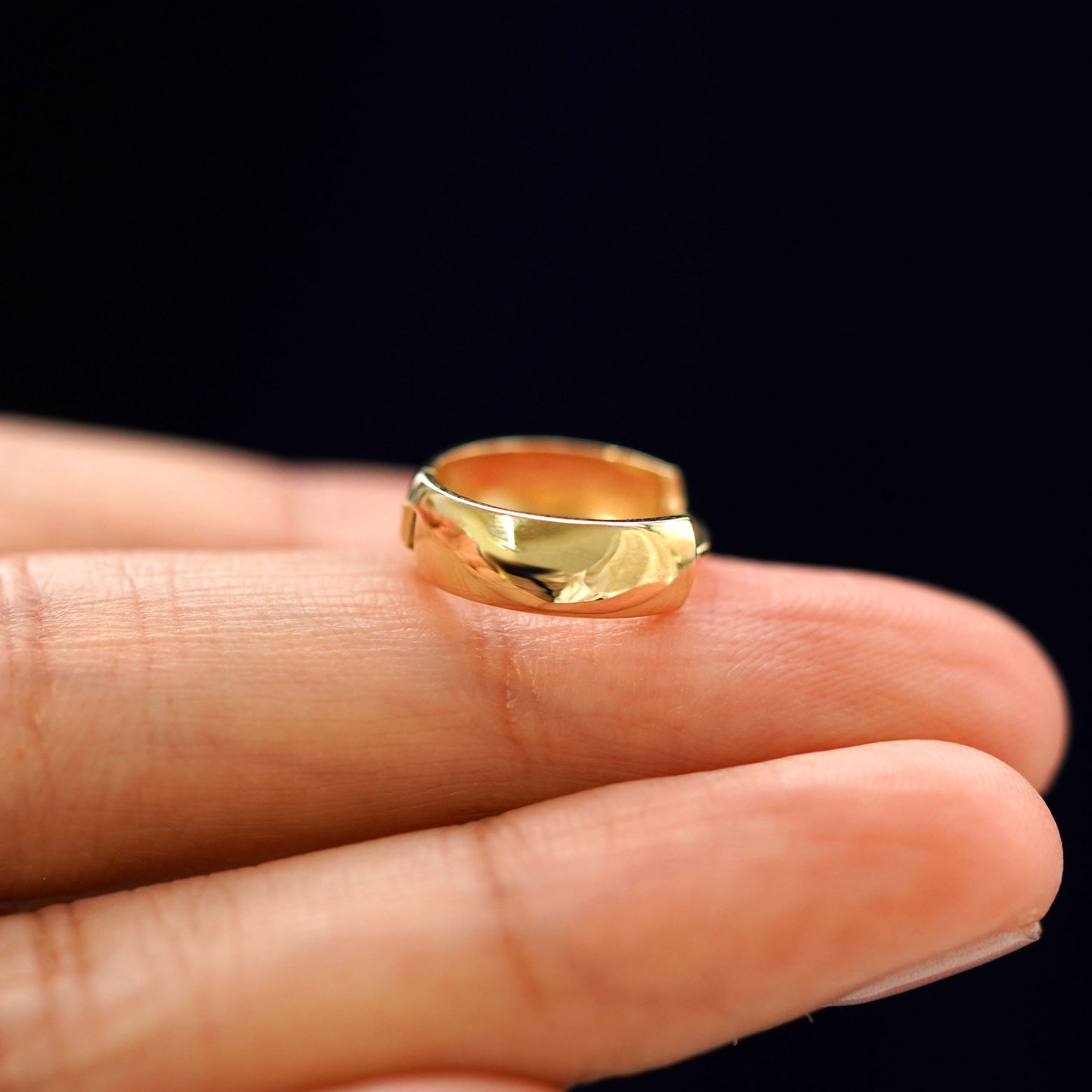 A yellow gold Medium Thick Huggie Hoop Earring laying sideways on a model's fingertips