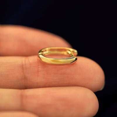 A 14 karat gold Wide Thick Huggie Hoop laying on a model's fingertips on it's side