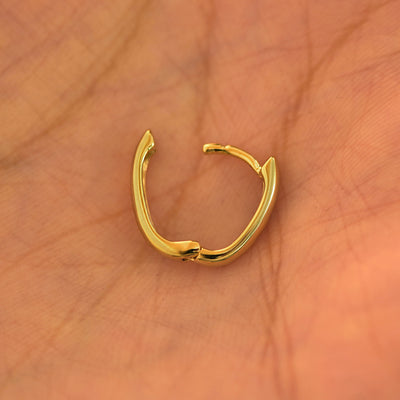 An open 14k yellow gold Thick Oval Huggie Hoop resting in a model's palm