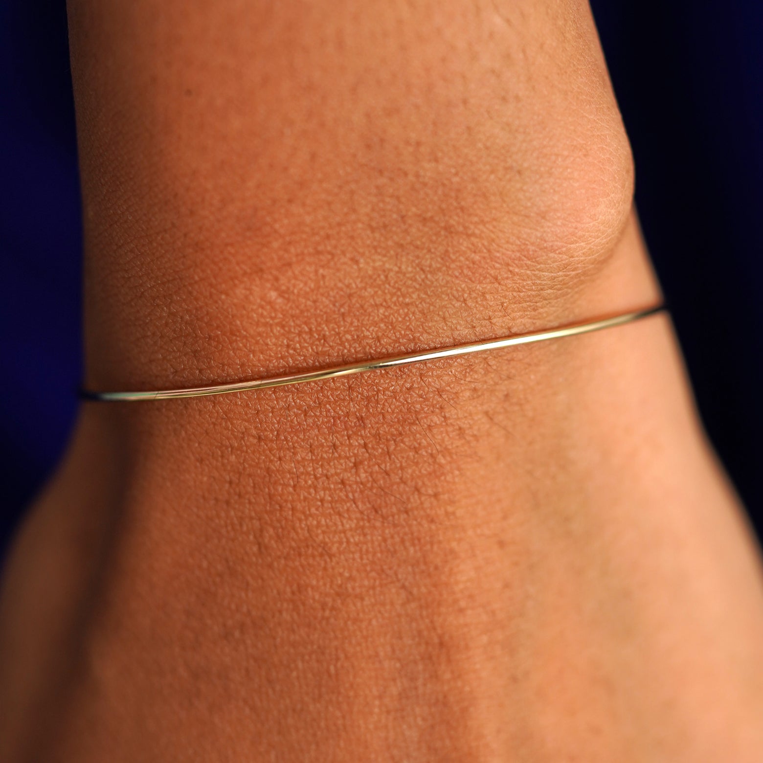 Close up view of a model's wrist wearing a yellow gold Line Bangle Bracelet