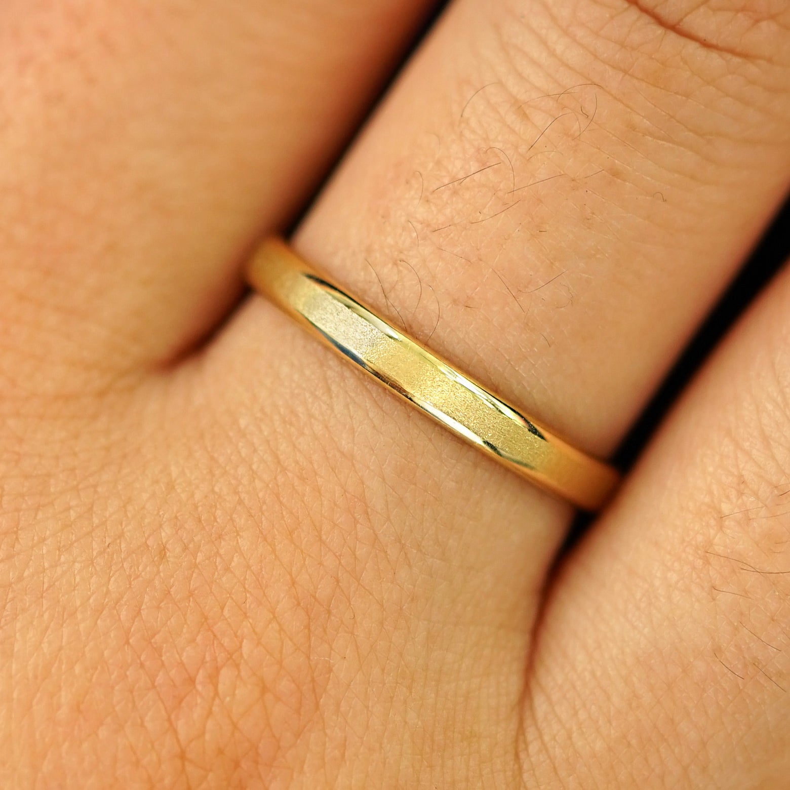 Close up view of a model's hand wearing a solid yellow gold Beveled Edge Band