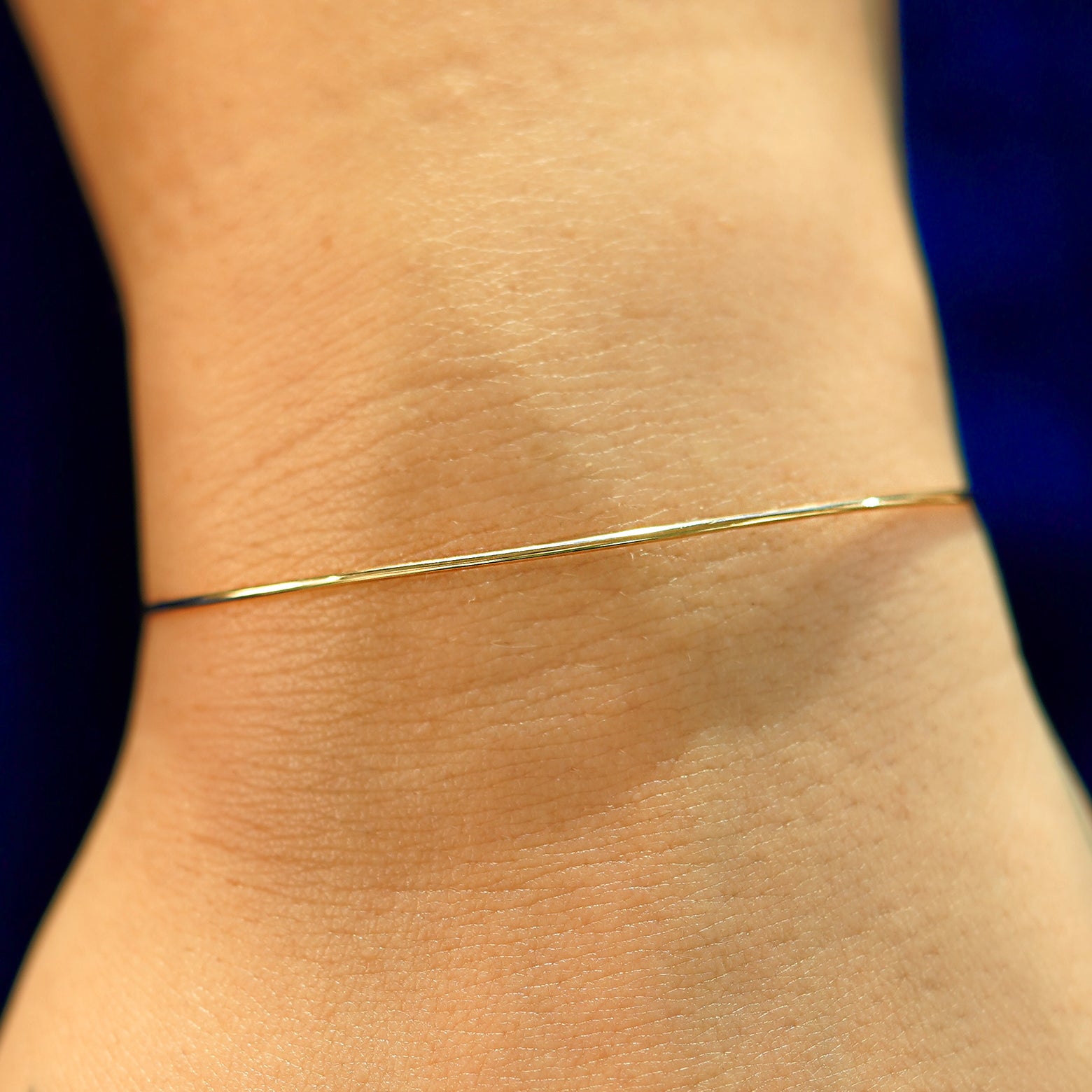 A model's wrist wearing a solid gold Line Bangle Bracelet