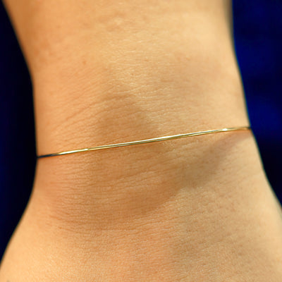 A model's wrist wearing a solid gold Line Bangle Bracelet