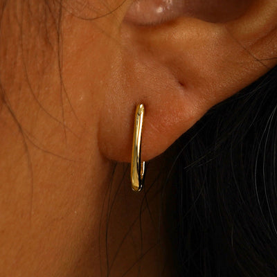 Close up view of a model's ear wearing a solid yellow gold Thin Oval Huggie Hoop