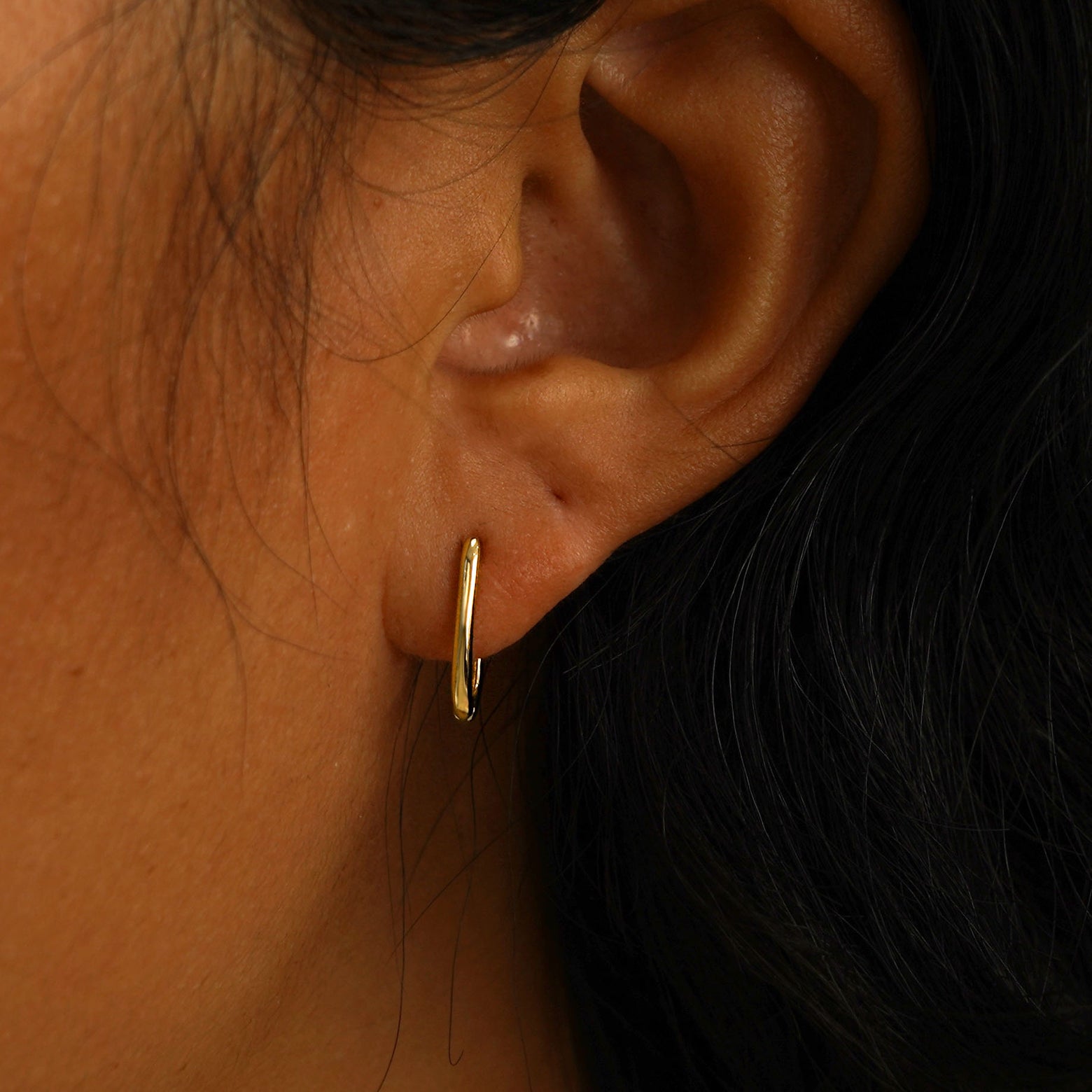 A model's ear wearing a 14 karat yellow gold Thin Oval Huggie Hoop