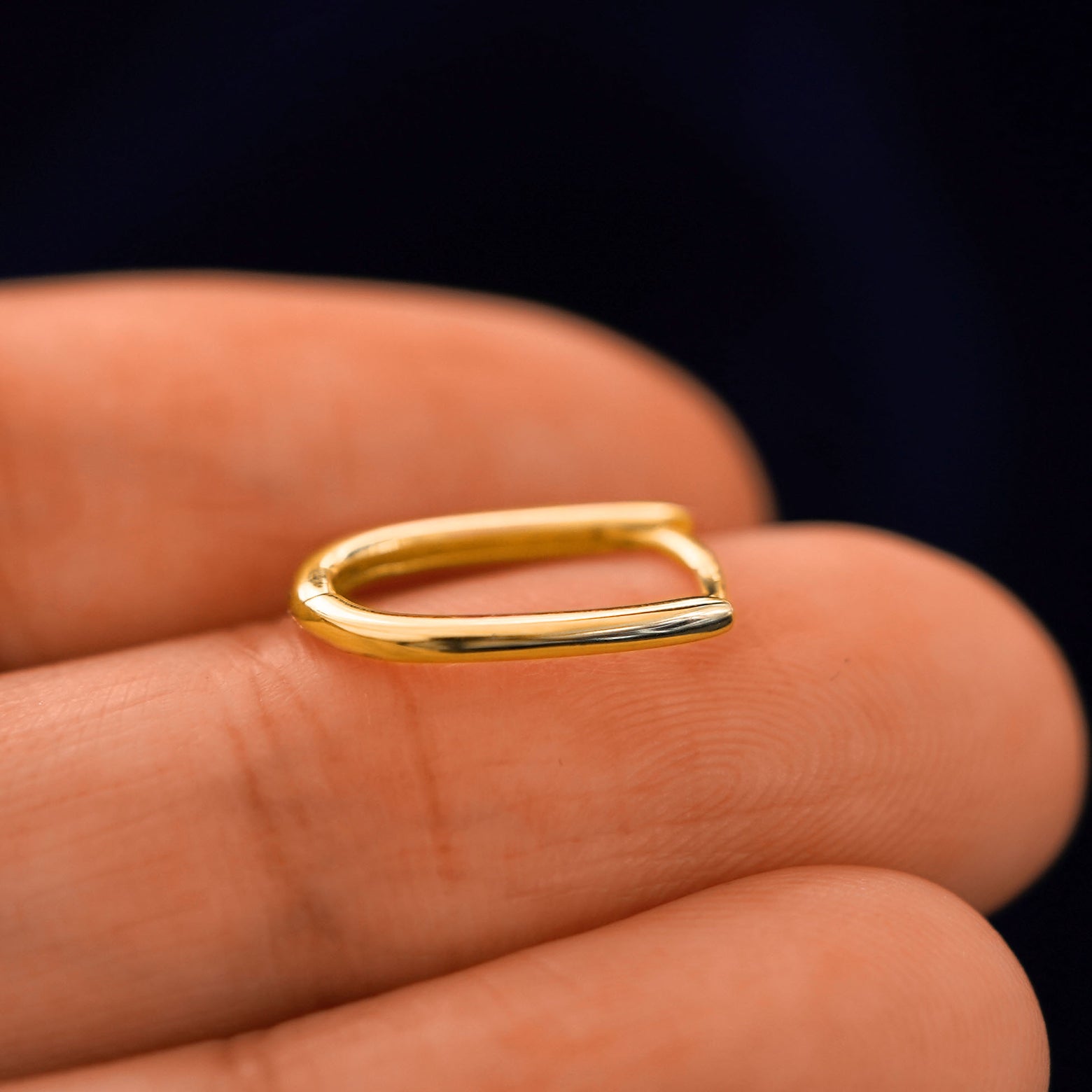 A 14 karat gold Thin Oval Huggie Hoop laying on a model's fingertips on it's side