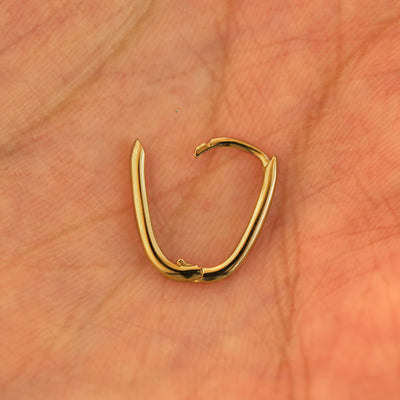 An open 14k yellow gold Thin Oval Huggie Hoop resting in a model's palm