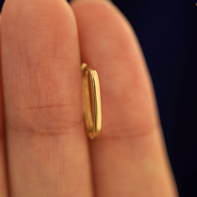 A 14k solid gold Thin Oval Huggie Hoop between a model's fingers to show the thickness of the earring