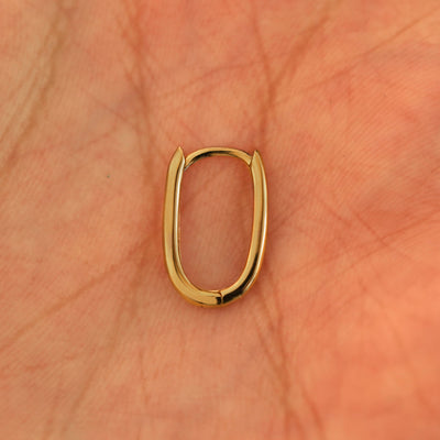 A single closed 14k yellow gold Thin Oval Huggie Hoop resting in a model's palm