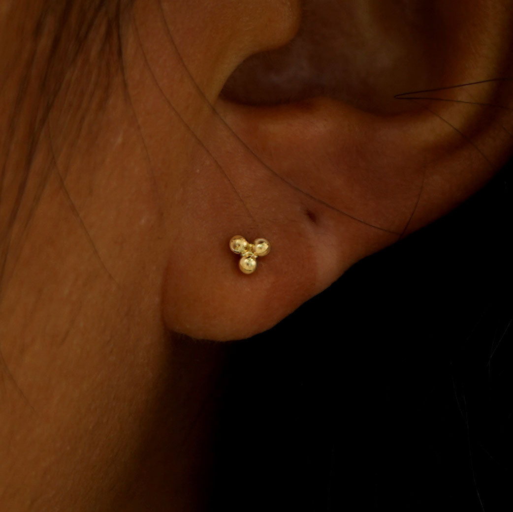 Close up view of a model's ear wearing a yellow gold Ball Trio Flatback Piercing