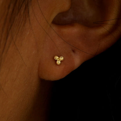 Close up view of a model's ear wearing a yellow gold Ball Trio Flatback Piercing