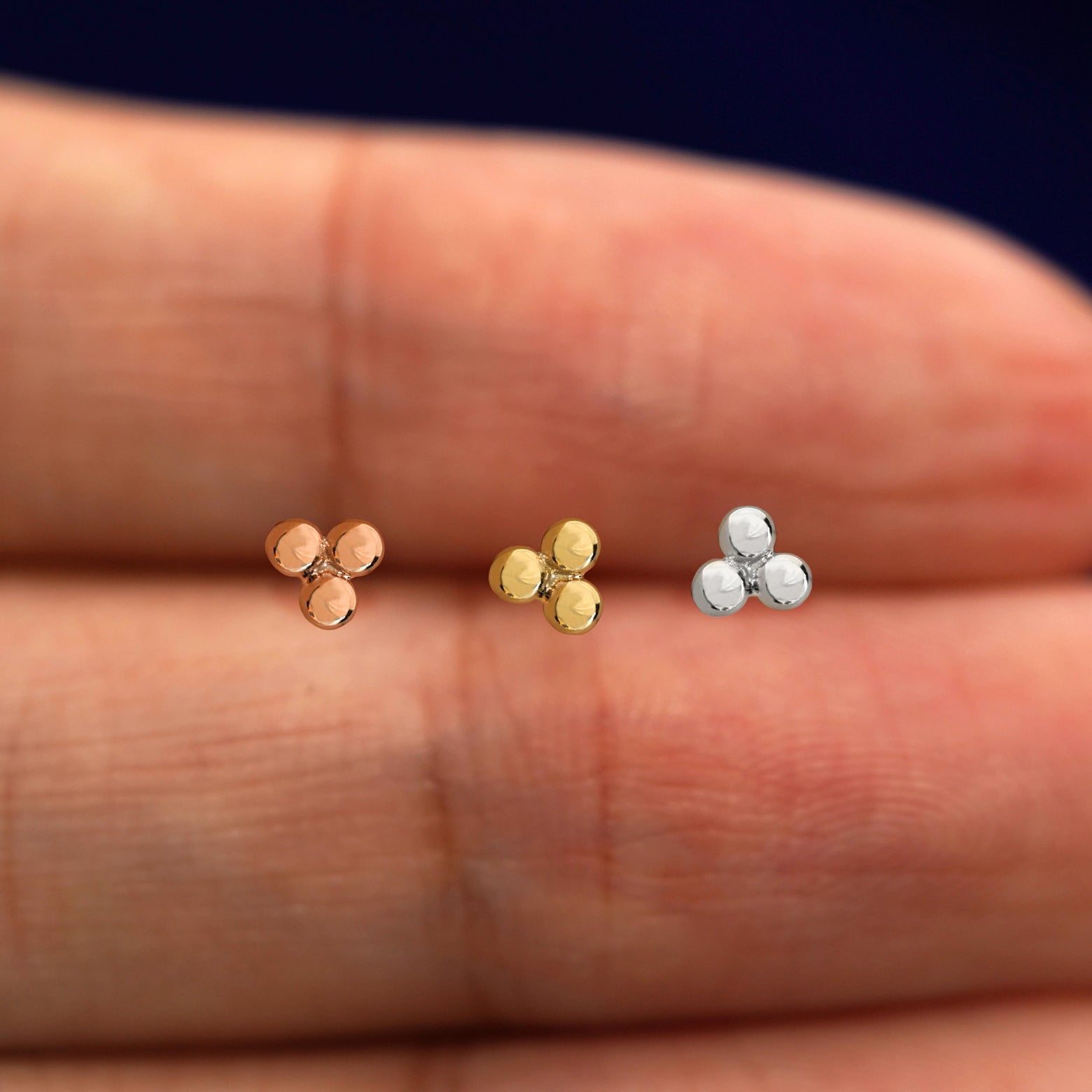 Three versions of the Ball Trio Flat Back showing options of yellow, rose, and white gold in between a model's fingers