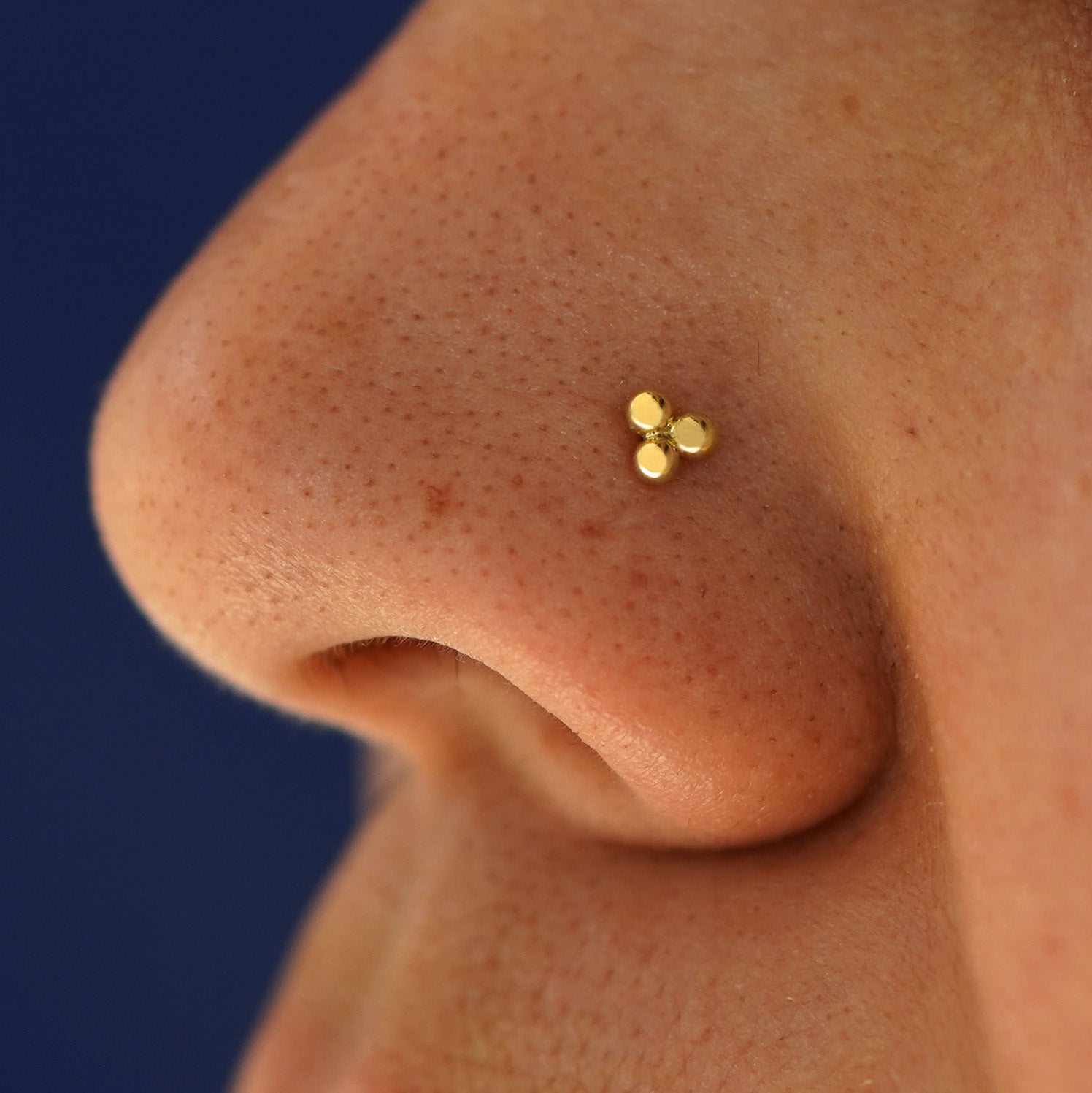 Close up view of a model's nose wearing a solid 14k yellow gold Ball Trio Nose Stud