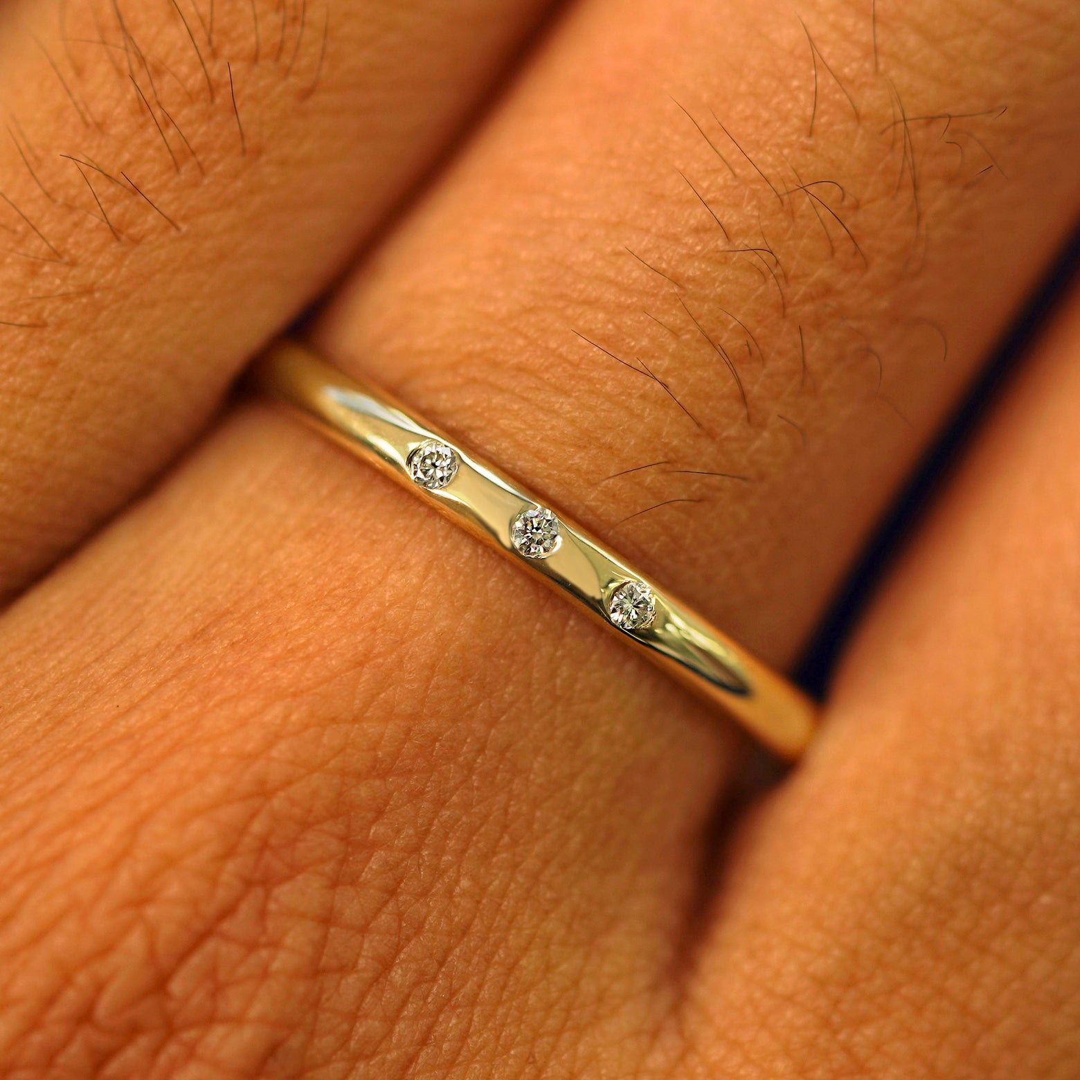 Close up view of a model's fingers wearing a yellow gold 2mm Curvy Mirror Band with three diamonds