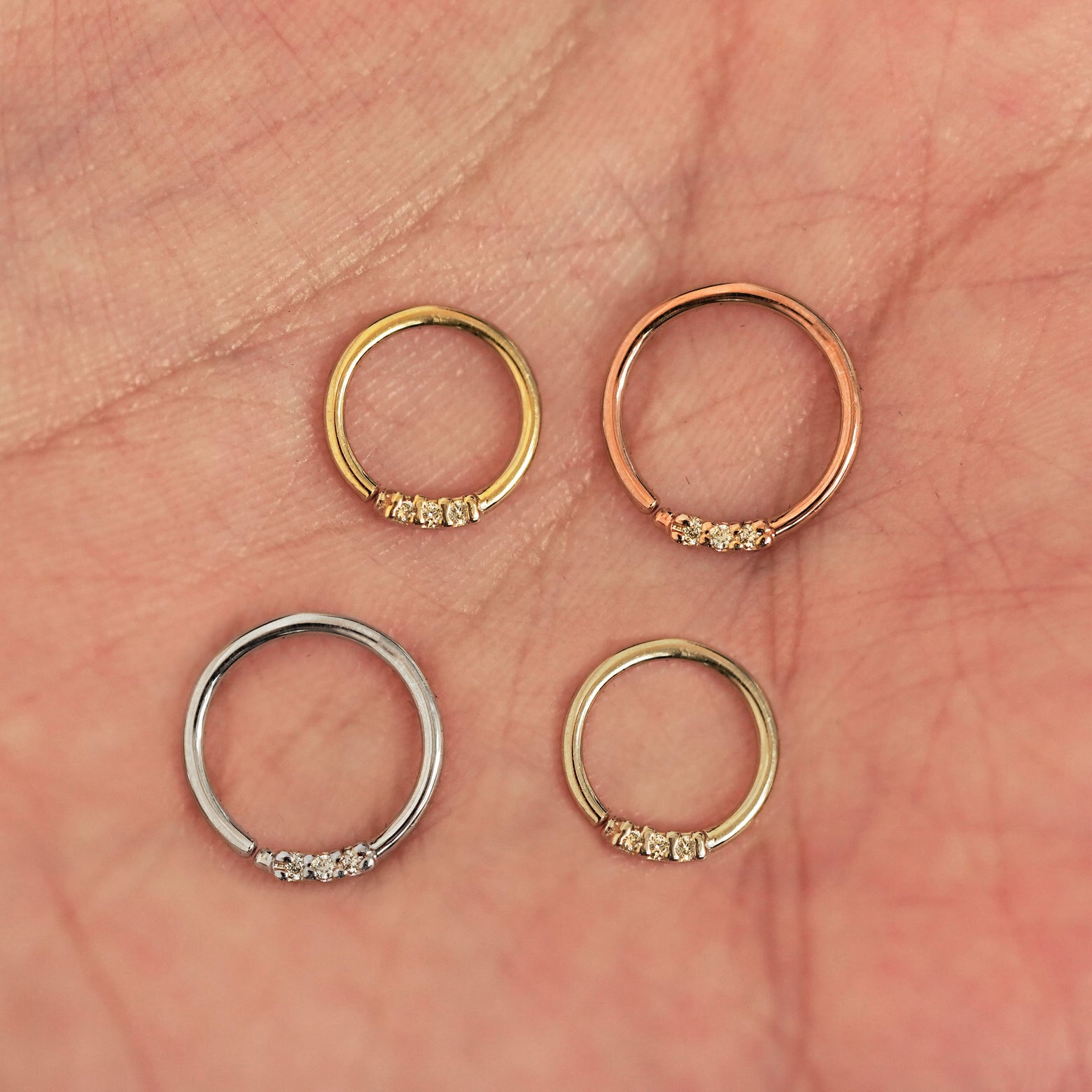 Four versions of the 3 Diamond Septum shown in options of yellow, white, rose and champagne gold in a model's palm