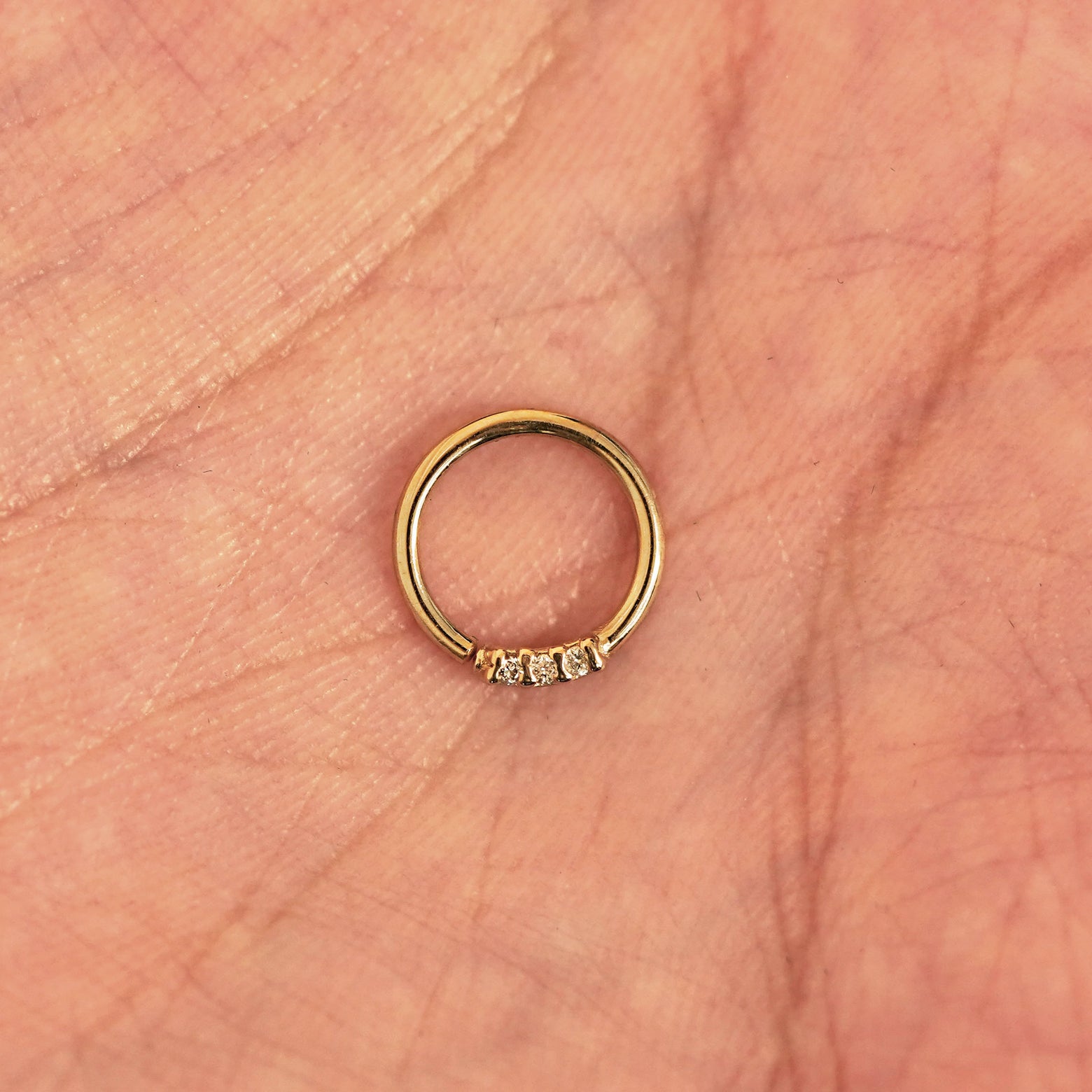 A model's hand holding a 14 karat yellow gold Pierced 3 Diamond Septum