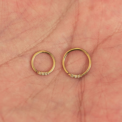 A model's palm holding two versions of the pierced 3 Diamond Septum showing the 8mm and 10mm sizes