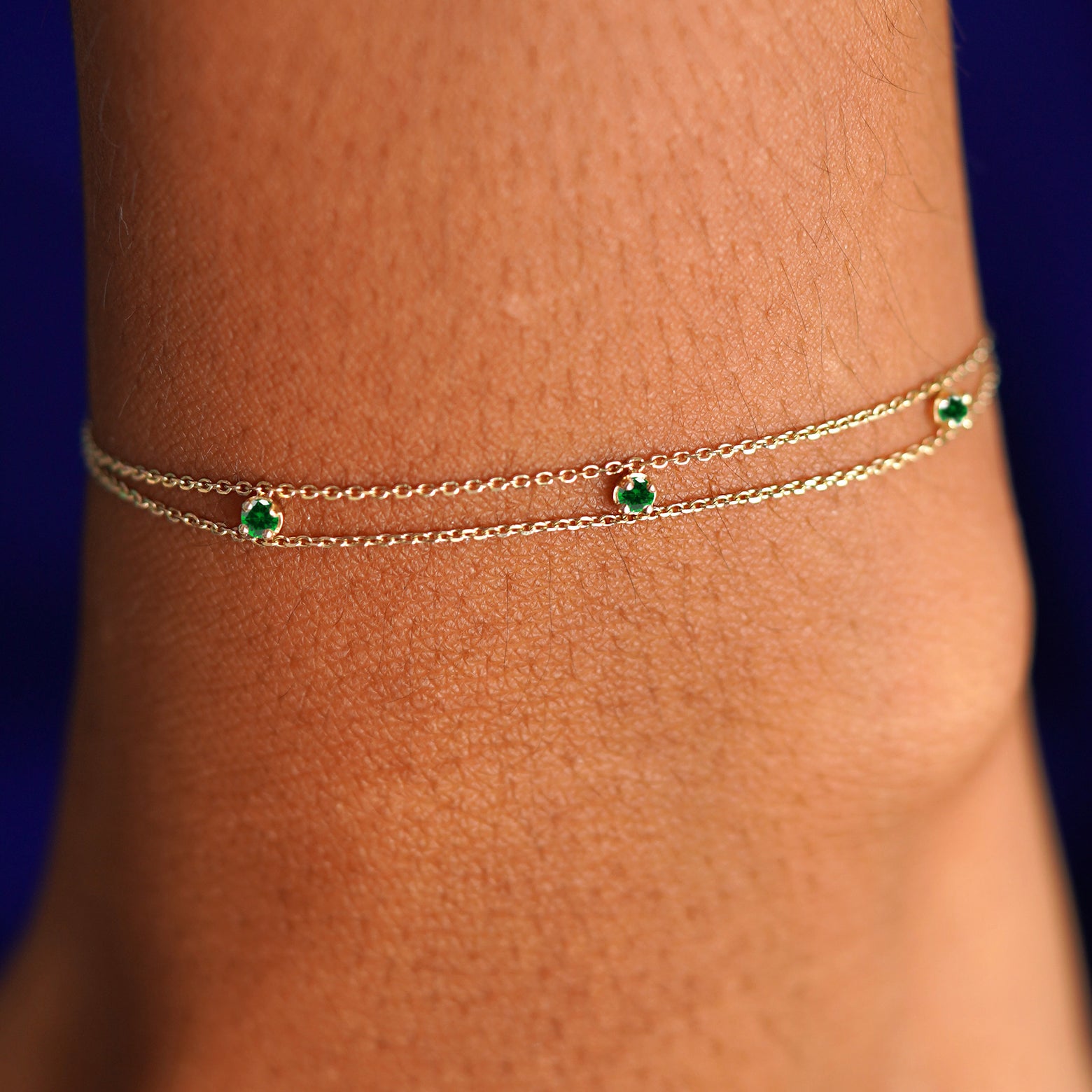 A model's wrist wearing a solid gold 3 Gemstone Cable Bracelet in emerald