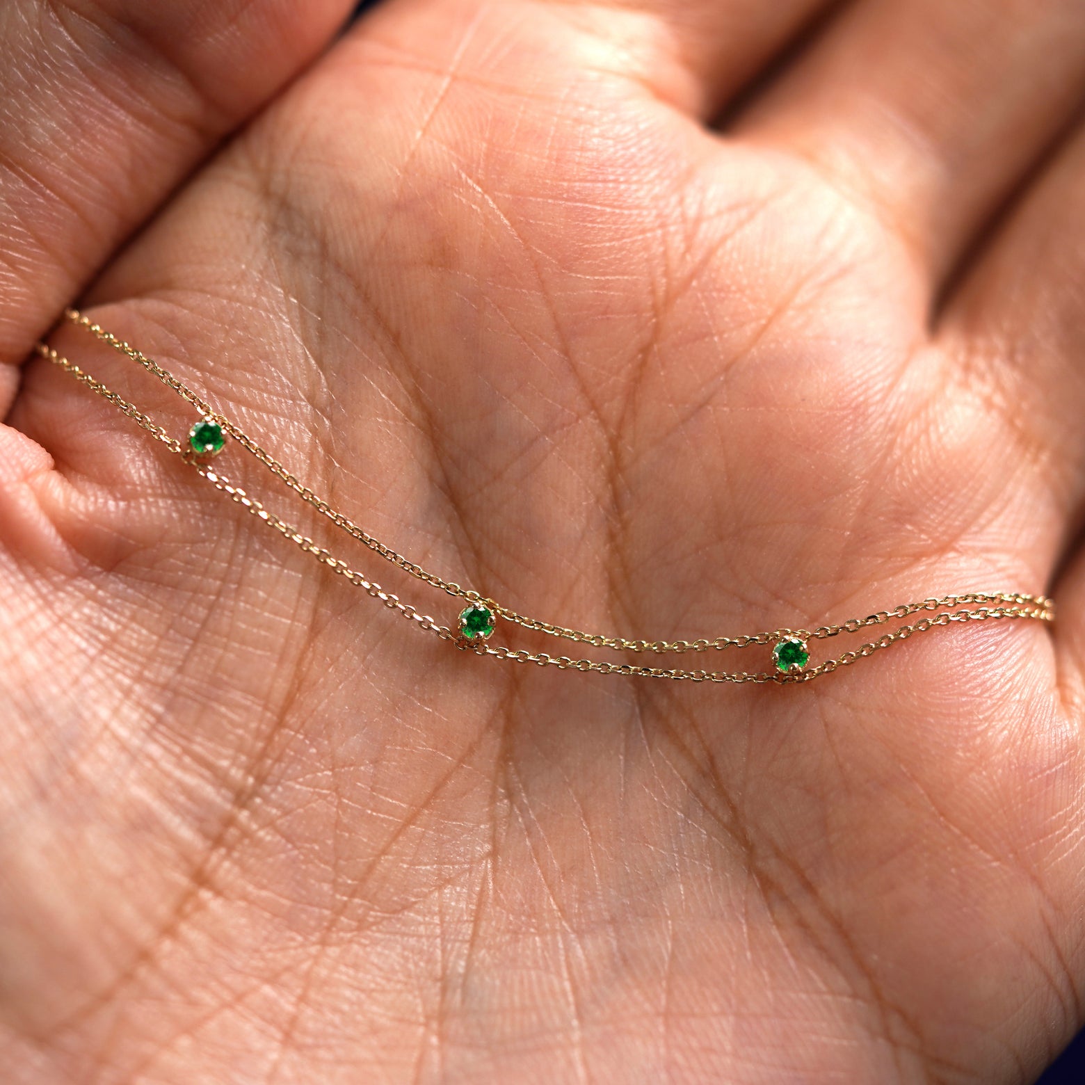 A yellow gold emerald 3 Gemstone Cable Bracelet draped on a model's palm