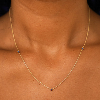 A model's neck wearing a solid 14k yellow gold 3 Gemstone Cable Necklace in sapphire