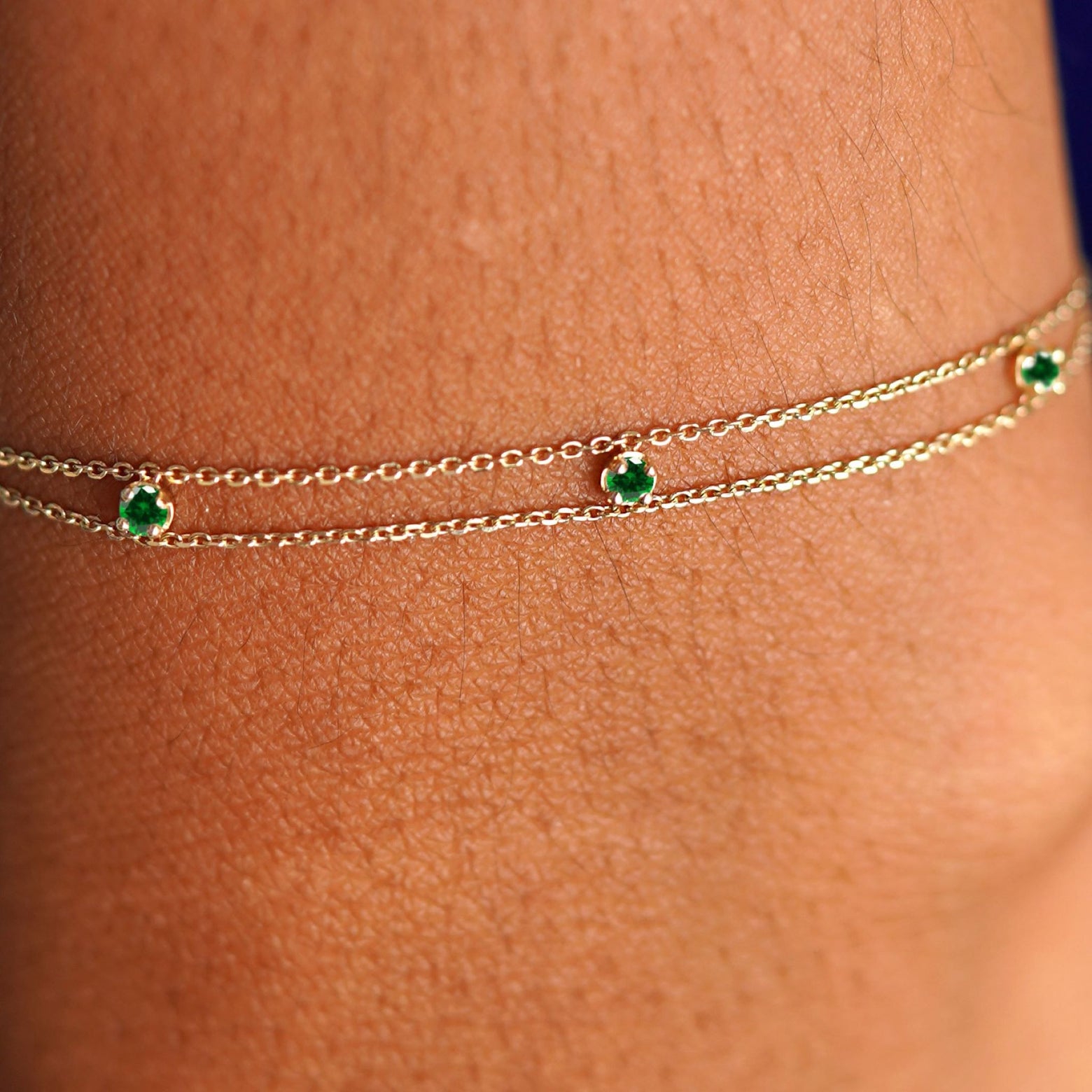 Close up view of a model's wrist wearing a solid gold 3 Gemstone Cable Bracelet in emerald