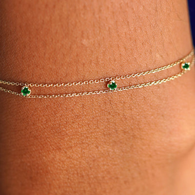 Close up view of a model's wrist wearing a solid gold 3 Gemstone Cable Bracelet in emerald