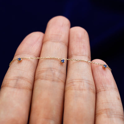 A yellow gold sapphire 3 Gemstone Cable Necklace resting on a model's fingers