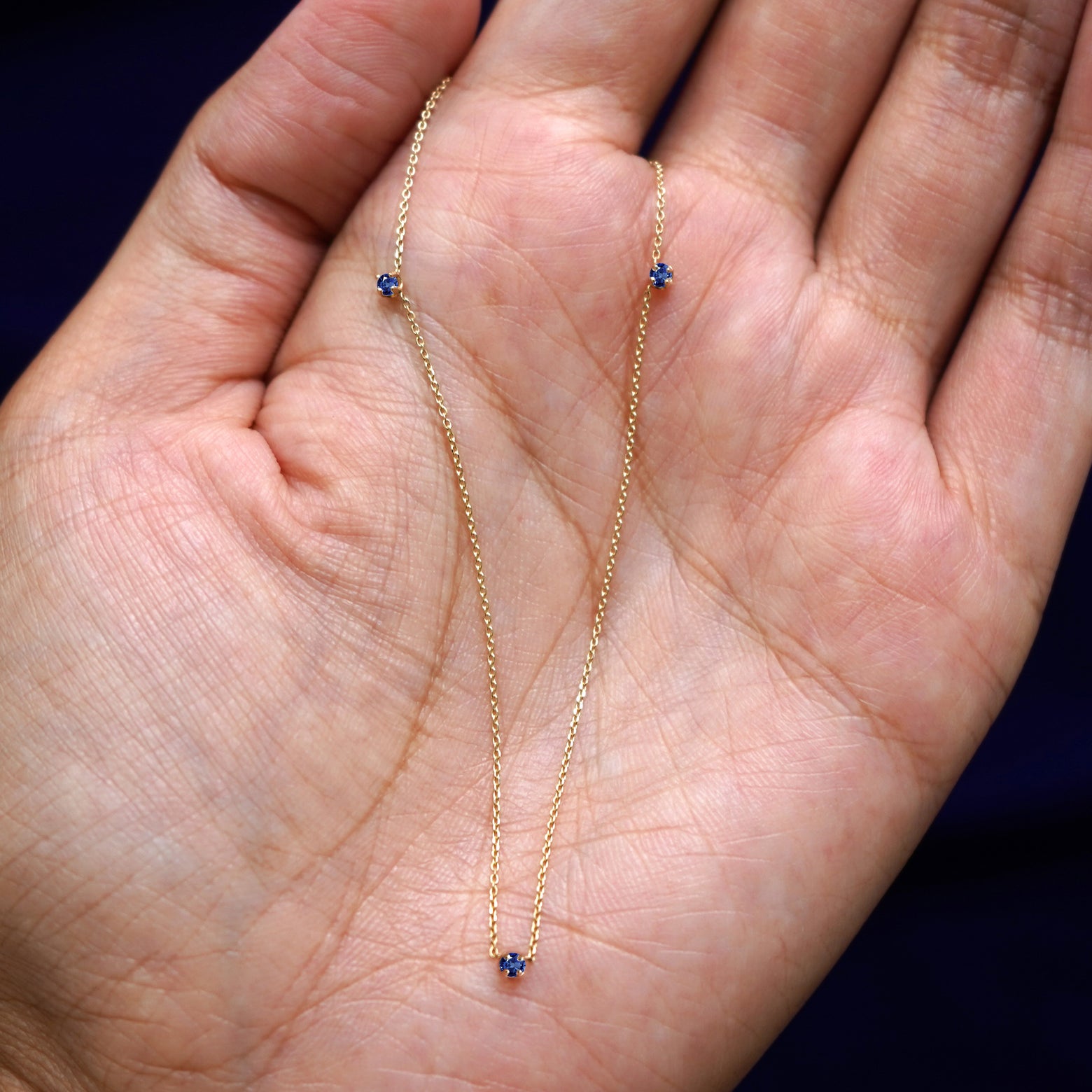 A yellow gold sapphire 3 Gemstone Cable Necklace draped on a model's palm