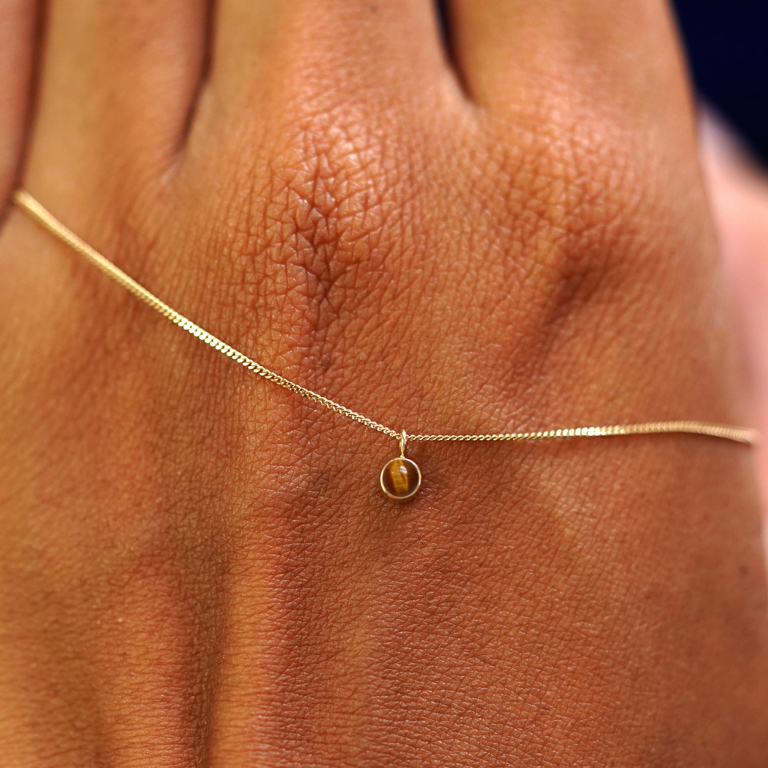 A solid yellow gold Tiger Eye Necklace draped across the back of a model's hand