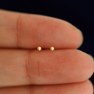 A pair of solid 14k yellow gold Mini Ball Flatback Piercing in between a model's fingers