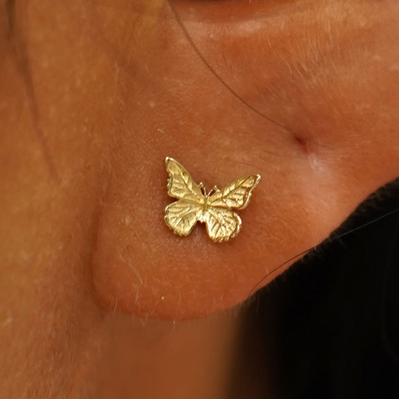 Close up view of a model's ear wearing a 14k yellow gold Mini Butterfly Earring