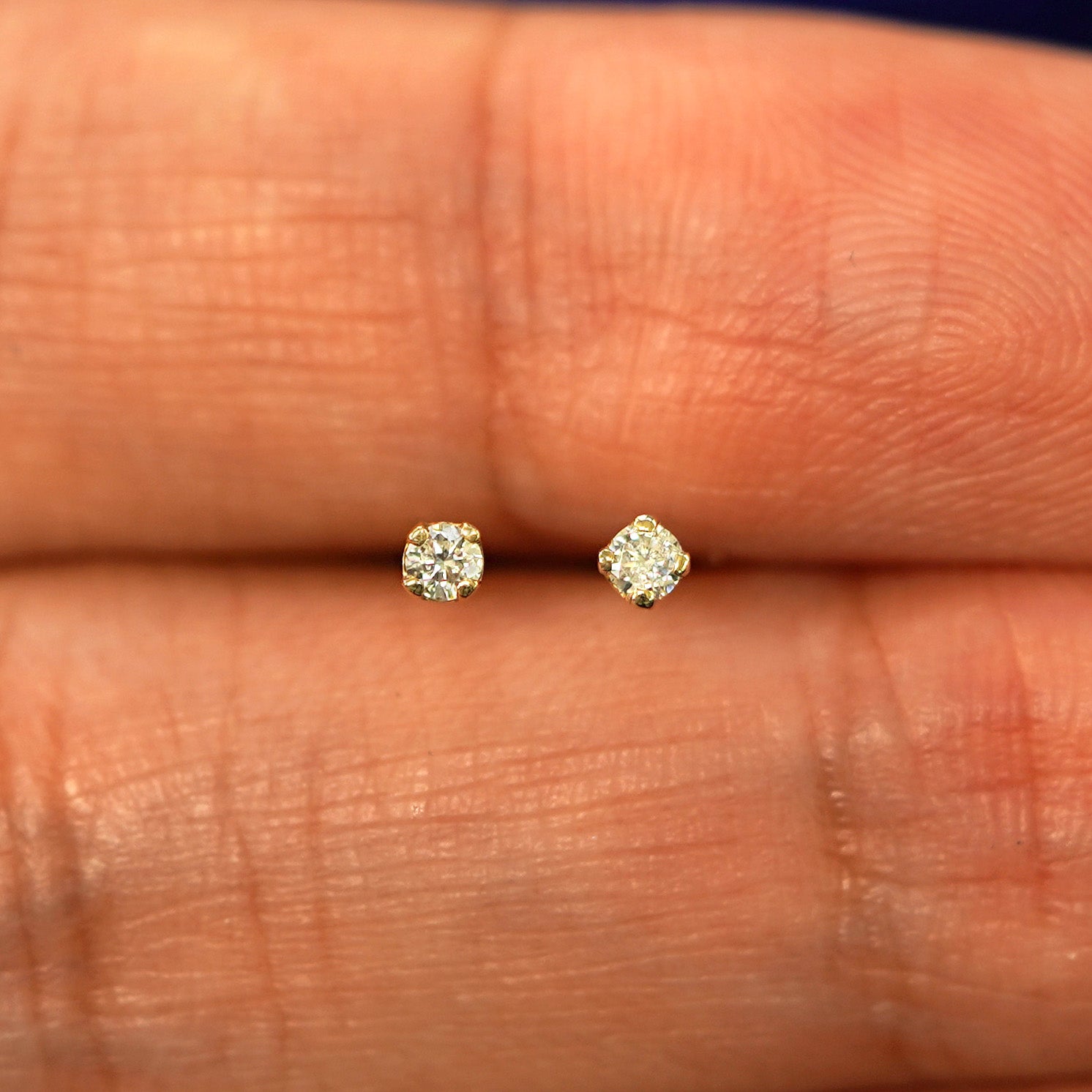 A pair of 14 karat gold studs earrings with 2 millimeter round 0.03ct Diamonds in between a models fingers