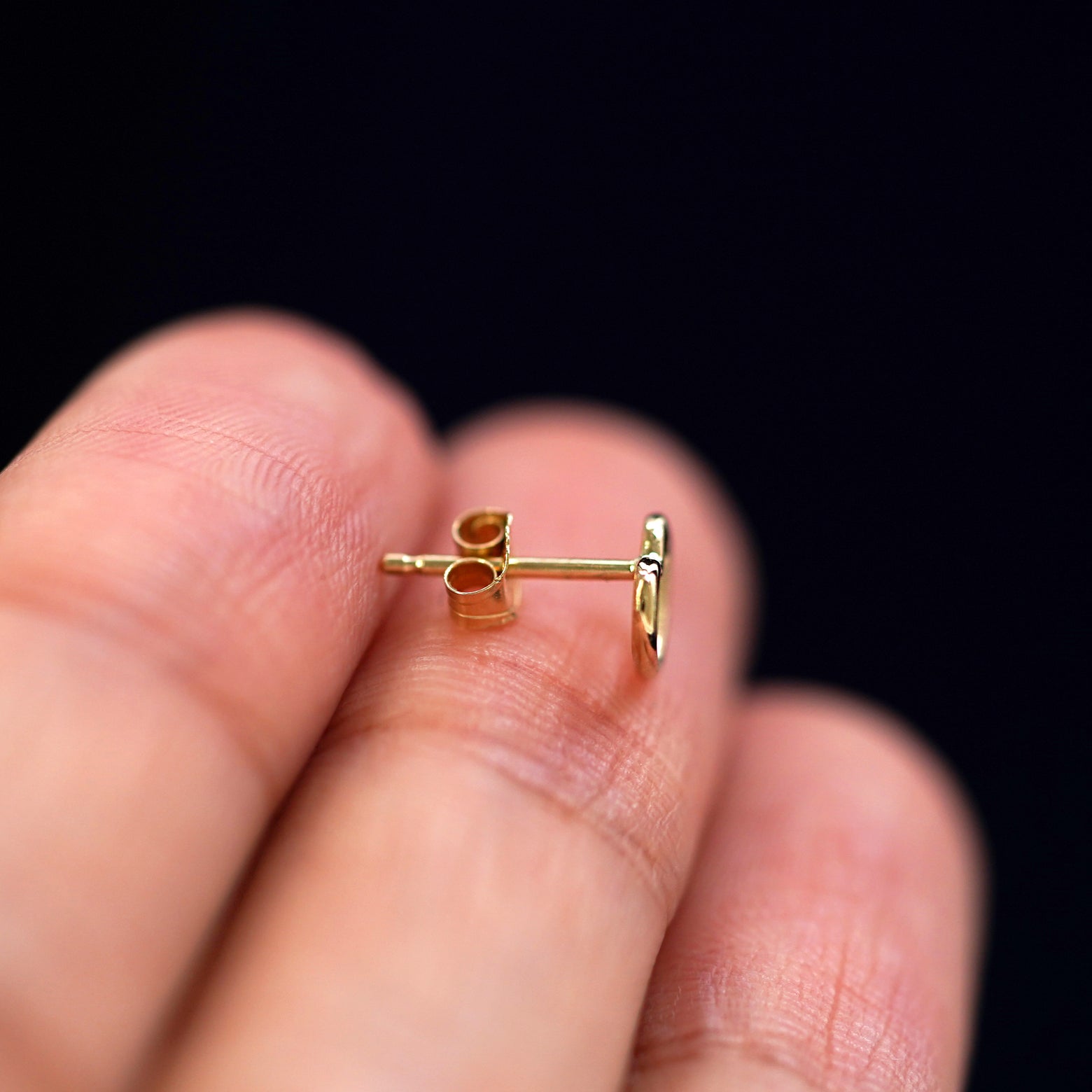 A 14k gold Heart Earring sitting sideways on a model's fingertips to show detail