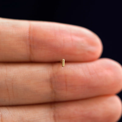 A solid 14k yellow gold Small Line Earring in between a model's fingers