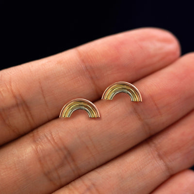 A model's hand holding a pair of recycled 14k gold Rainbow Earrings