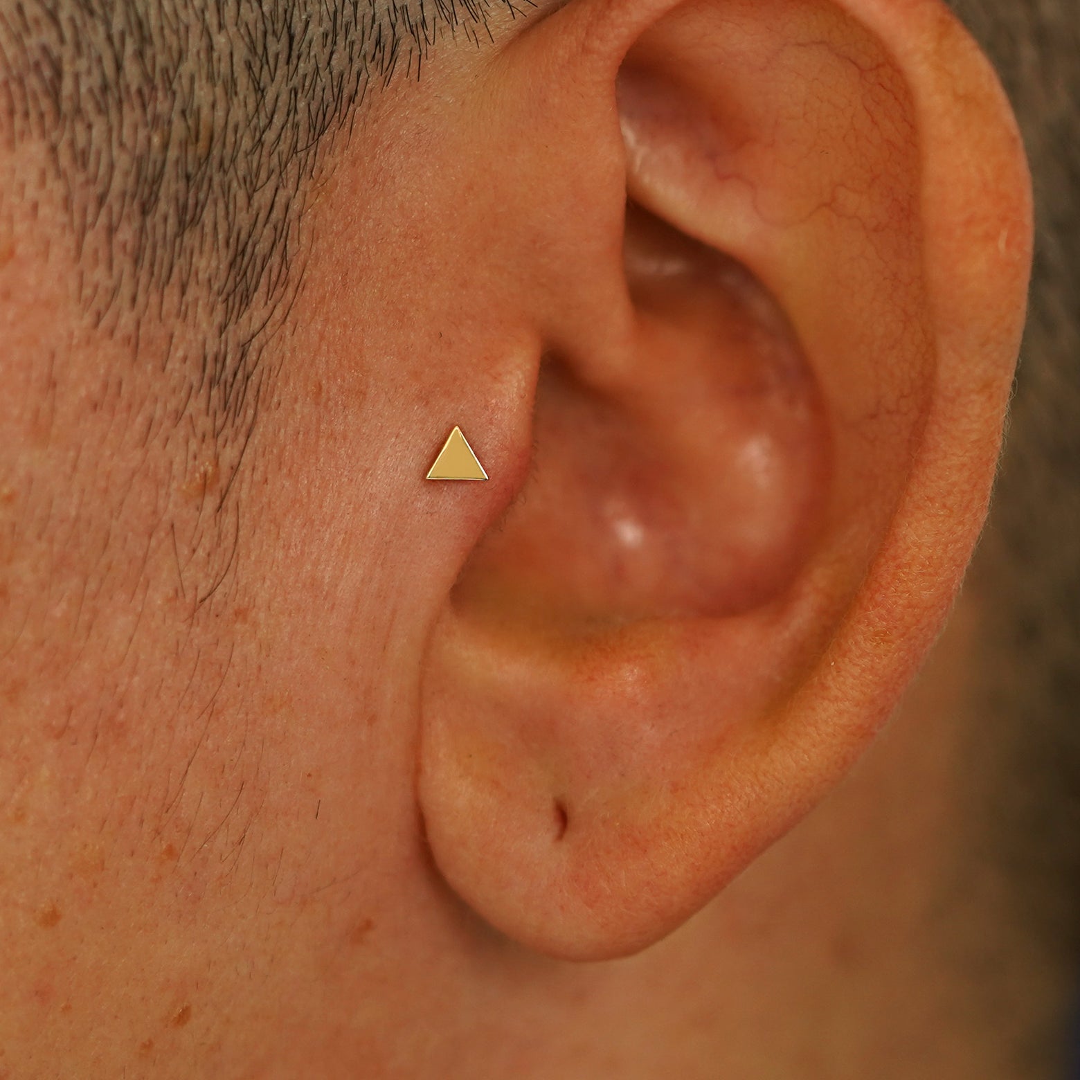 Close up view of a model's ear wearing a yellow gold Triangle Flatback in a tragus piercing