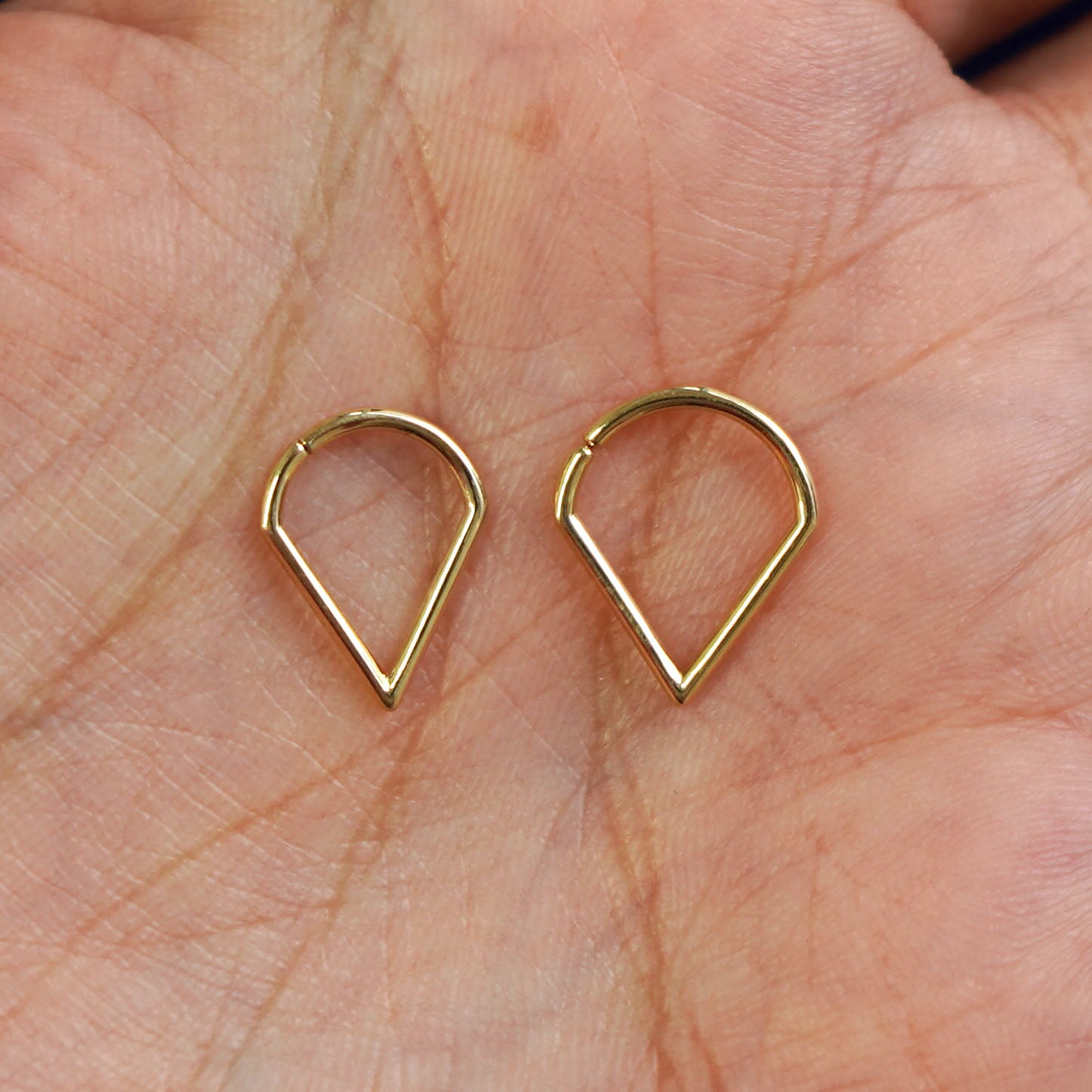 A model's palm holding two versions of the pierced Triangle Septum showing the 8mm and 10mm sizes