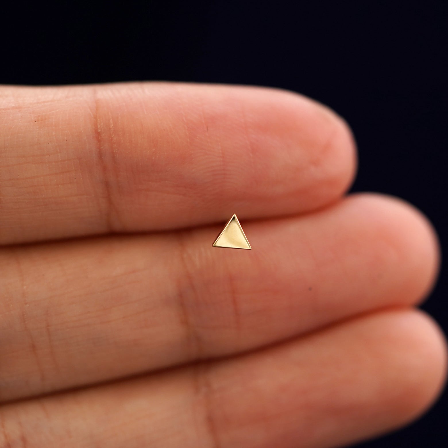 A solid 14k yellow gold Triangle Earring in between a model's fingers